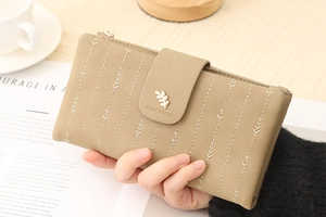 Detail of a beige PU leather wallet featuring leaf embroidery and a gold leaf metal clasp