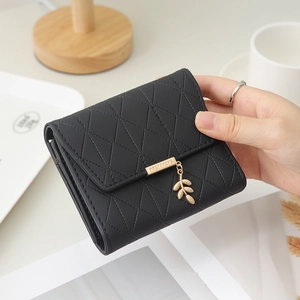 Détail du portefeuille noir matelassé avec pendentif en feuille dorée et finitions chic