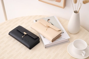Detail of long leather wallets in black and beige with gold heart pendants and multi-slots