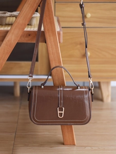 Gros plan du sac bandoulière vintage en cuir marron avec coutures blanches et boucle en D