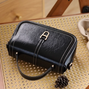 Détail du sac en cuir noir texturé avec fermoir doré et surpiqûres blanches contrastées
