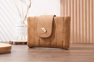 Brown short PU leather wallet with leaf charm and floral embroidery on wooden table