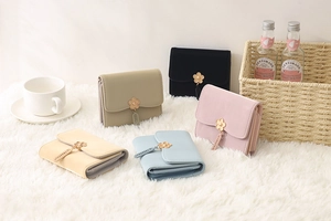 Close-up of five colorful tri-fold PU leather wallets with cute flower charms on a rug