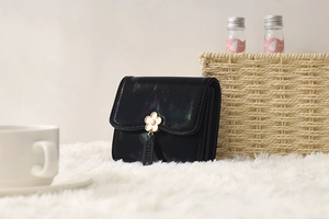 Close-up of black holographic tri-fold wallet with flower charm on white plush rug