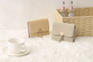 Detail of short tri-fold wallets in cream and green with flower charms and PU leather