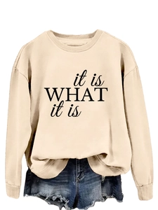 Detail eines beigen Crewneck-Sweatshirts mit schwarzem 'it is what it is' Schriftzug