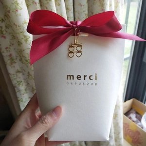White textured gift box with red satin bow, gold charm, and merci beaucoup text