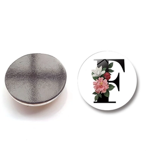 Detail of round magnetic fridge sticker with floral letter F and magnetic back view