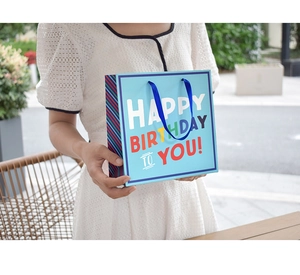 Blue Happy Birthday gift bag with ribbon handles and colorful striped side panels
