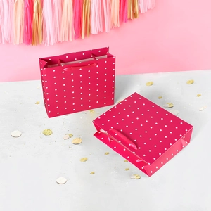 Pink polka dot gift bags with satin ribbon handles in a festive party setting