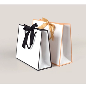 Detail of white paper gift bags with elegant black and orange borders and ribbon handles
