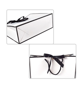 Detail of minimalist white gift bag featuring black ribbon bow and reinforced bottom folding