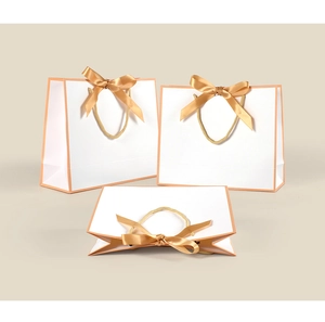 Macro detail of white gift bags with pink trim, golden satin bow and braided rope handles
