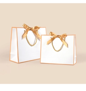 Detail of white gift bags with orange piping and decorative gold satin bows on handles
