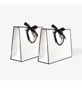 Detail of white paper gift bags with black trim and elegant satin bow handles