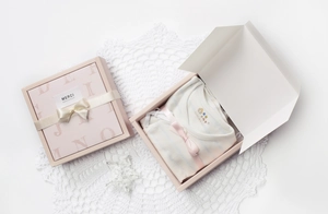 Detail of pink striped baby clothes inside a premium gift box with ribbon and Merci tag