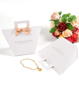 Weiße Geschenktüte in Trapezform mit rosa Satinschleife und goldenem Tragegriff
