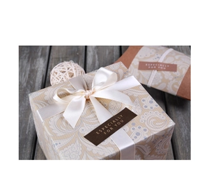 Detalle de caja de regalo paisley beige con lazo de satén y sello de pan de oro