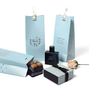 Blue gift bag with gold foil 'Thank you' text and white ribbon handles in a flat lay setup