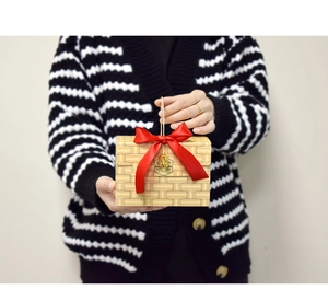 Detail of faux rattan gift box with red silk bow and elegant golden charms in hand