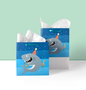 Close-up of blue gradient cartoon shark gift bags with satin handles and white tissue paper