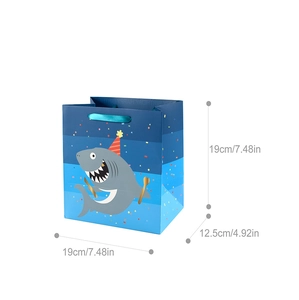 Detail view of cartoon shark birthday gift bag with blue silk handles and happy birthday text