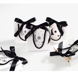 Detail view of small white gift bags featuring black bow and celestial moon line art
