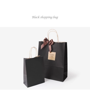 Detail of matte black kraft paper gift bags with brown satin bow and thank you label