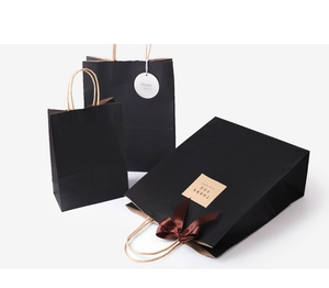 Detail of matte black paper gift bags with handles, silk bow, and Thank You label