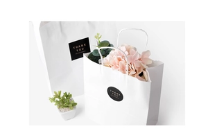 Detailed view of white gift bag with gold Thank You sticker and pink floral decor