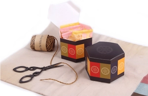 Dettaglio scatola regalo esagonale con motivi floreali e dolci gourmet all'interno