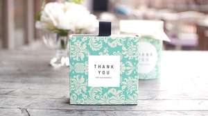 Details von minzgrüner Geschenkbox und Dose mit Blumenmuster, schwarzem Band und Etikett