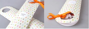 Detalle de caja de regalo con gotas de colores, cinta naranja y etiqueta de gracias