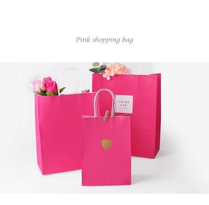 Three sizes of rose pink paper gift bags with white handles and a golden heart detail