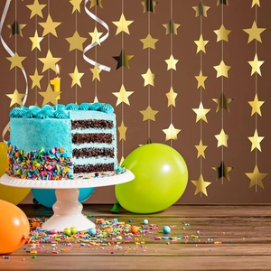Close-up of golden star garlands hanging above a birthday cake with festive decor
