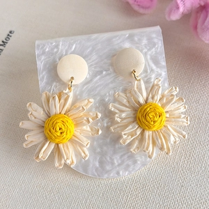 Close-up of handmade woven daisy earrings with white raffia petals and yellow centers