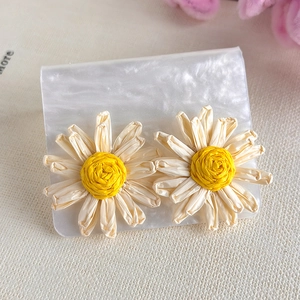Detailed macro view of handmade cream daisy earrings with woven yellow center on white card