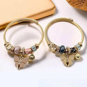 Detail of golden steel cable bracelet featuring pearl bow charms and butterfly pendant