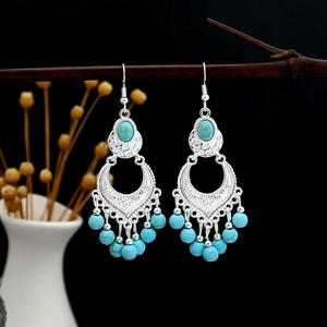 Artistic close-up of Bohemian turquoise tassel earrings hanging on a dry branch