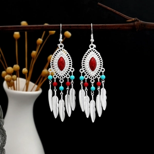 Close-up of Bohemian silver leaf tassel earrings with red turquoise stone on wooden branch