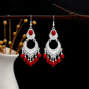 Detail of bohemian silver earrings with red stone inlay and tassels on a branch