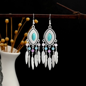 Detail of bohemian drop earrings with turquoise stones and silver feather tassels on wood