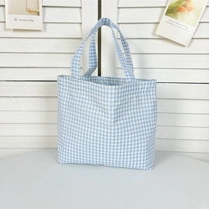 Detail of light blue checkered canvas tote bag on a white table with a clean rustic backdrop
