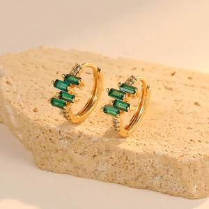 Macro shot of gold-plated hoop earrings with rectangular green zircons on a stone surface