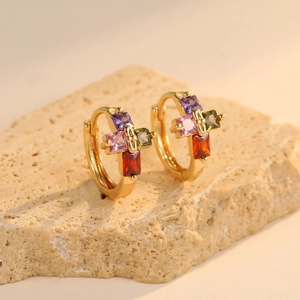Gold-plated hoop earrings with colorful gemstone clusters on a beige stone surface