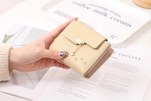 Close-up of beige trifold wallet with heart pendant and textured faux leather finish