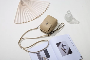 Détail du sac de téléphone beige avec grain de litchi, logo et bandoulière