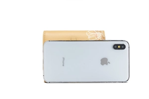 Dettaglio del portafoglio in pelle gialla con stampa floreale rispetto a uno smartphone