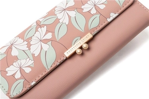Detail of floral print PU leather flap and gold metal buckle on a pink tri-fold wallet