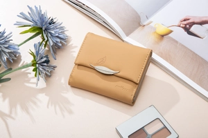 Detail of a tri-fold wallet with a silver metal leaf buckle and brand logo on a soft background